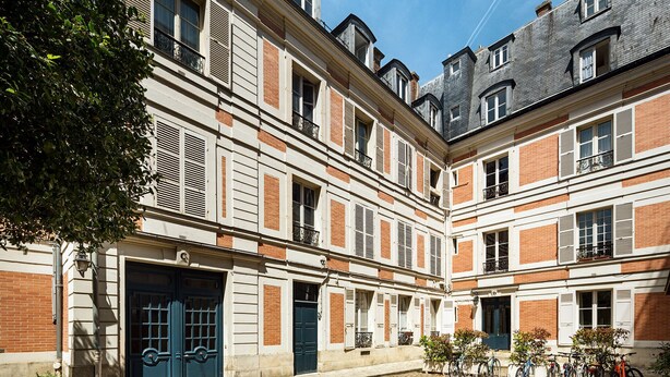 Un edificio histórico con un patio, que cuenta con una entrada de puertas dobles, múltiples ventanas y una fila de bicicletas estacionadas afuera.