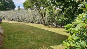 Un jardín bien cuidado con césped, setos frondosos y diversas especies de árboles.
