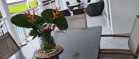 A modern outdoor dining area with a glass table, wicker chairs, and a potted plant.