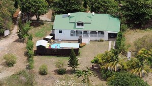 Una casa de dos pisos con techo verde, un porche cubierto y una piscina pequeña.