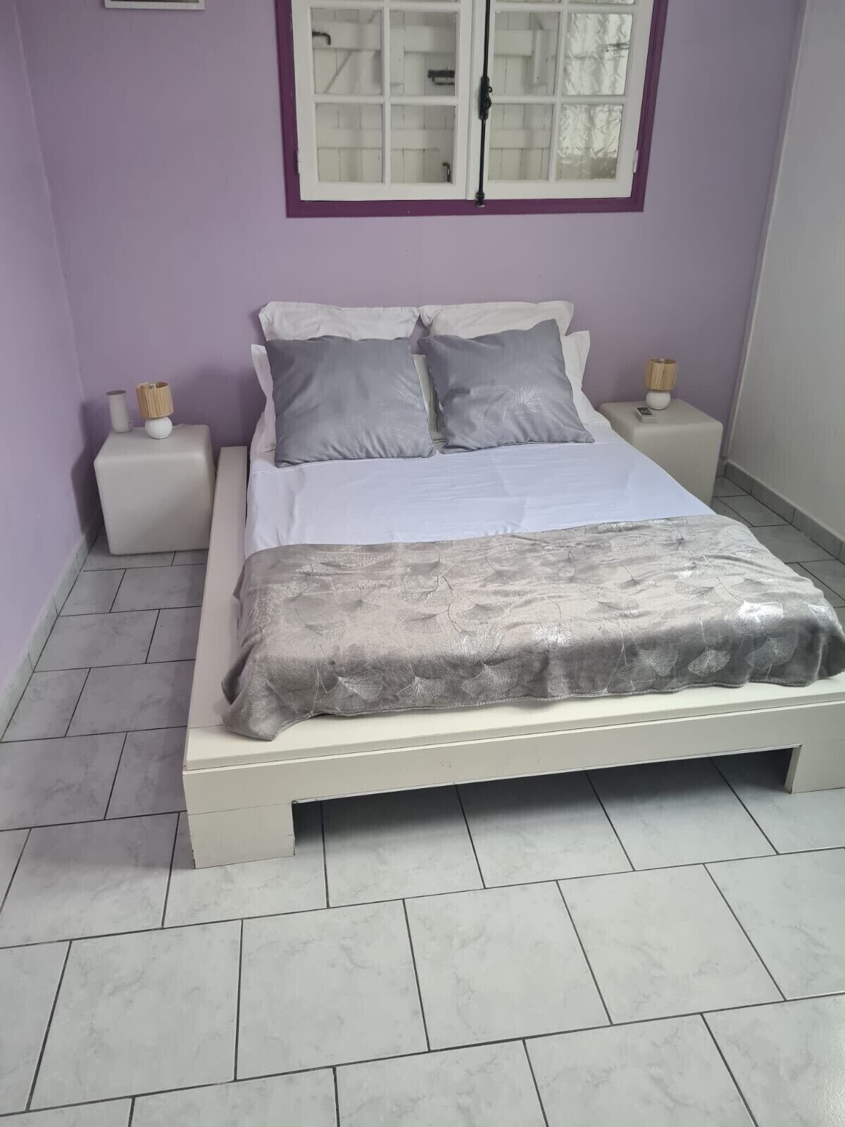 A bedroom with a bed, two bedside tables, a window, and a tiled floor.