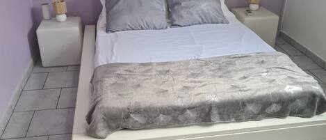 A bedroom with a bed, two bedside tables, a window, and a tiled floor.