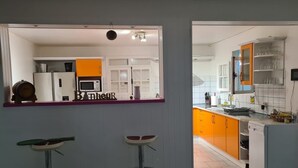 Una cocina moderna con armarios blancos y anaranjados, un microondas y un lavabo. Hay dos taburetes en primer plano.