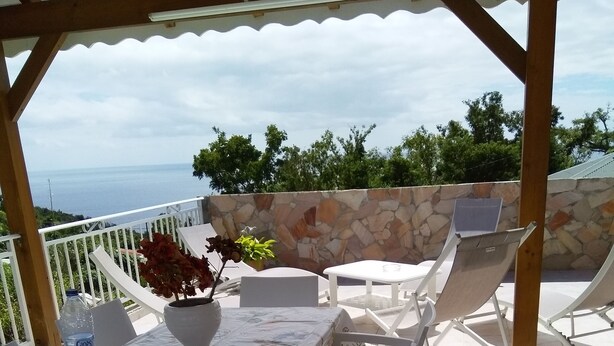An outdoor patio with a table set for dining, surrounded by white chairs, a potted plant, and a bottle of water. - HAUT DE VILLA VIEUX FORT (VIEUX FORT)