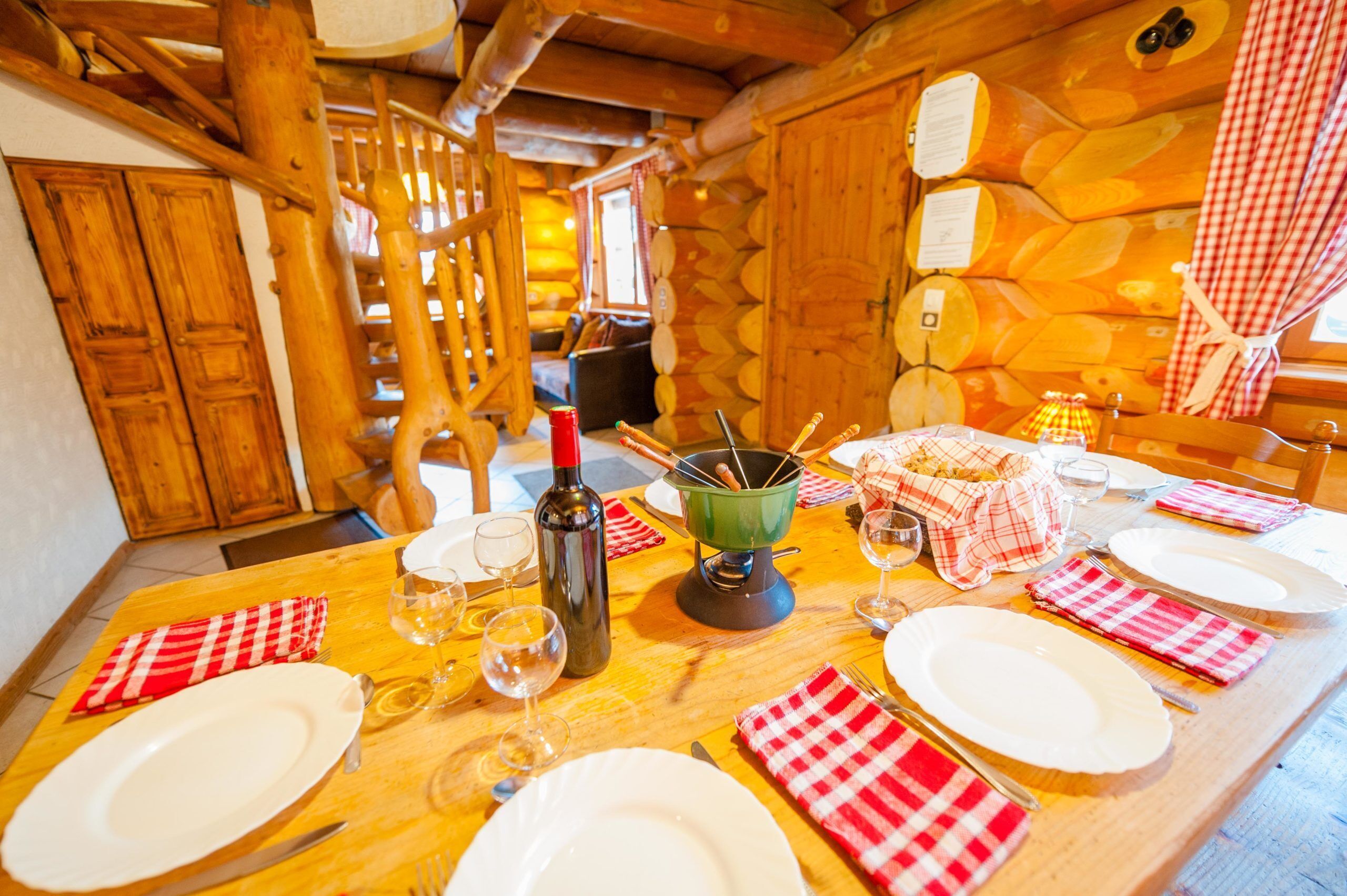 A wooden dining table set with plates, cutlery, wine glasses, and a bottle.