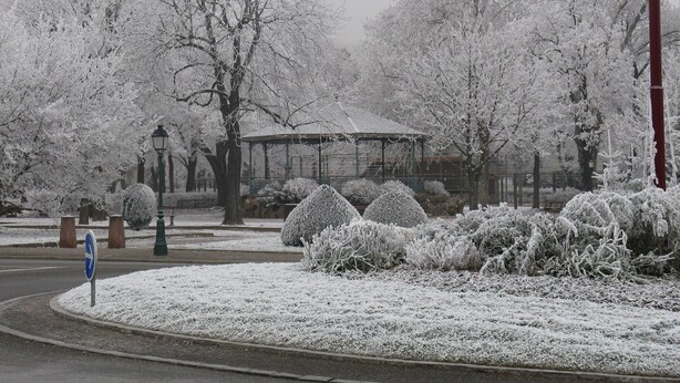 Een park bedekt met sneeuw, met een kiosk, bomen en een lantaarn.