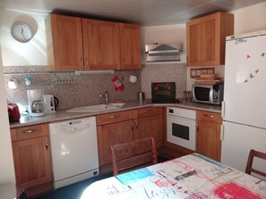 Una cocina compacta con armarios de madera, microondas integrado, cafetera y un lavamanos.