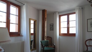 Een kamer met houten vloeren, een groene stoel, een tafel met een lamp en twee ramen voorzien van gordijnen.