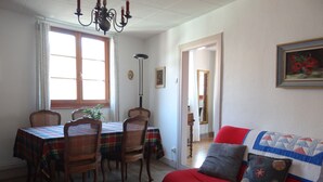 Een eethoek met een tafel voor vier personen, houten stoelen en een rode bank met decoratieve kussens.
