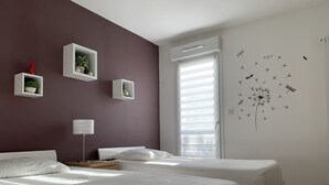A modern bedroom with two beds, a potted plant, and a wall decal of insects.