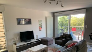 A modern living room with a flat-screen TV, a white coffee table, a grey sofa, and a red chair.