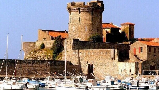 A historic stone castle with a tower, surrounded by a harbor with several boats.