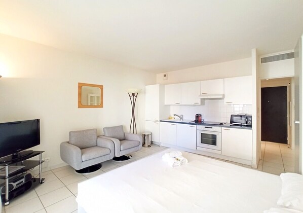 A modern hotel room with a flat-screen TV, a grey sofa, a dining area with a microwave, and a kitchenette. - Modern and Cosy Studio with Balcony (Cannes)