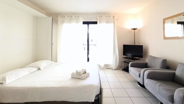 Una habitación de hotel con cama, sofá, televisión y ventana con cortinas.