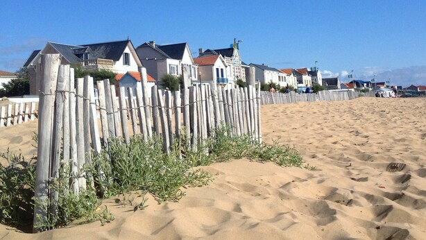 Ein Sandstrand mit Holzzäunen und Häusern im Hintergrund.
