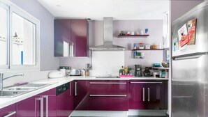 Eine moderne Küche mit lilafarbenen Schränken, einem Edelstahl-Kühlschrank und einem Fenster mit Blick auf eine verschneite Landschaft.