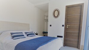 A neatly made bed with patterned pillows, a blue throw blanket, and a wooden door.