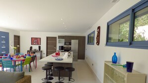 A modern kitchen with a central island, bar stools, and a dining area with colorful chairs and a table.
