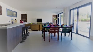 A modern kitchen with a dining area, large windows, and a flat-screen TV.