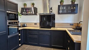 Una cocina moderna con armarios oscuros, electrodomésticos de acero inoxidable, encimera de madera y dos plantas en la pared.
