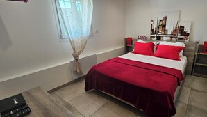 Un dormitorio con cama, ventana con cortinas, un cuadro en la pared y una pared de acento roja.