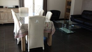 Un comedor con una mesa de vidrio y sillas de mimbre, un sofá de cuero negro y un mueble de madera.