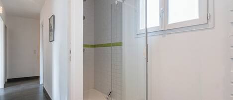 A bathroom with a glass shower enclosure, white tiled walls, and a window.
