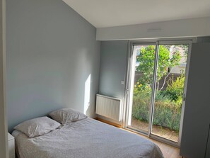 A bedroom with a bed, a radiator, and a sliding glass door to a garden.