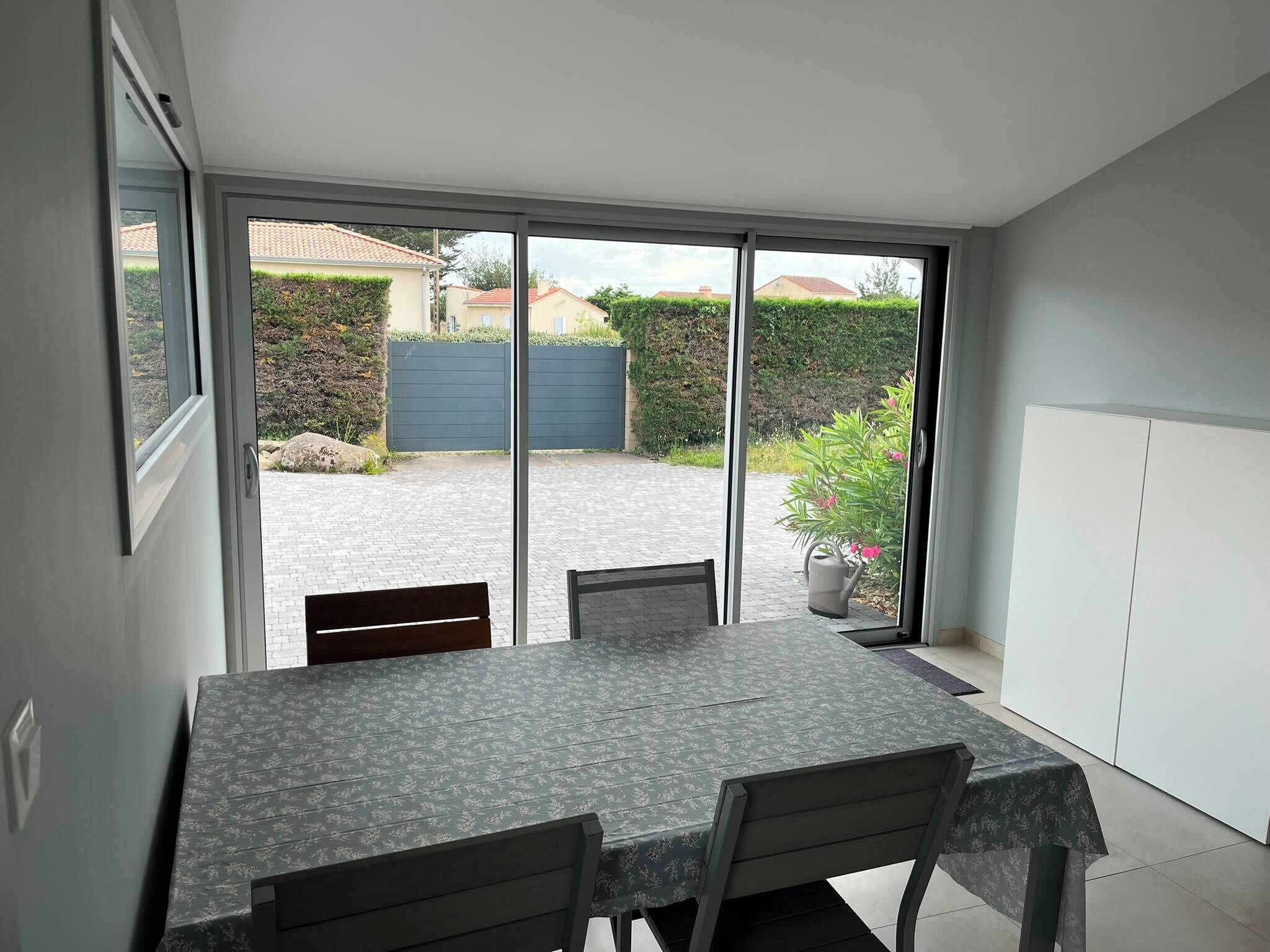 Un comedor con una mesa y sillas, un ventanal corredero que da a un patio con vistas a una zona residencial.
