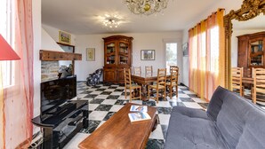 Uma sala de estar com piso xadrez, uma mesa de jantar de madeira com cadeiras, um lustre e um espelho grande.