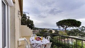 Varanda com mesa posta para dois, cadeiras brancas e vista para a paisagem.