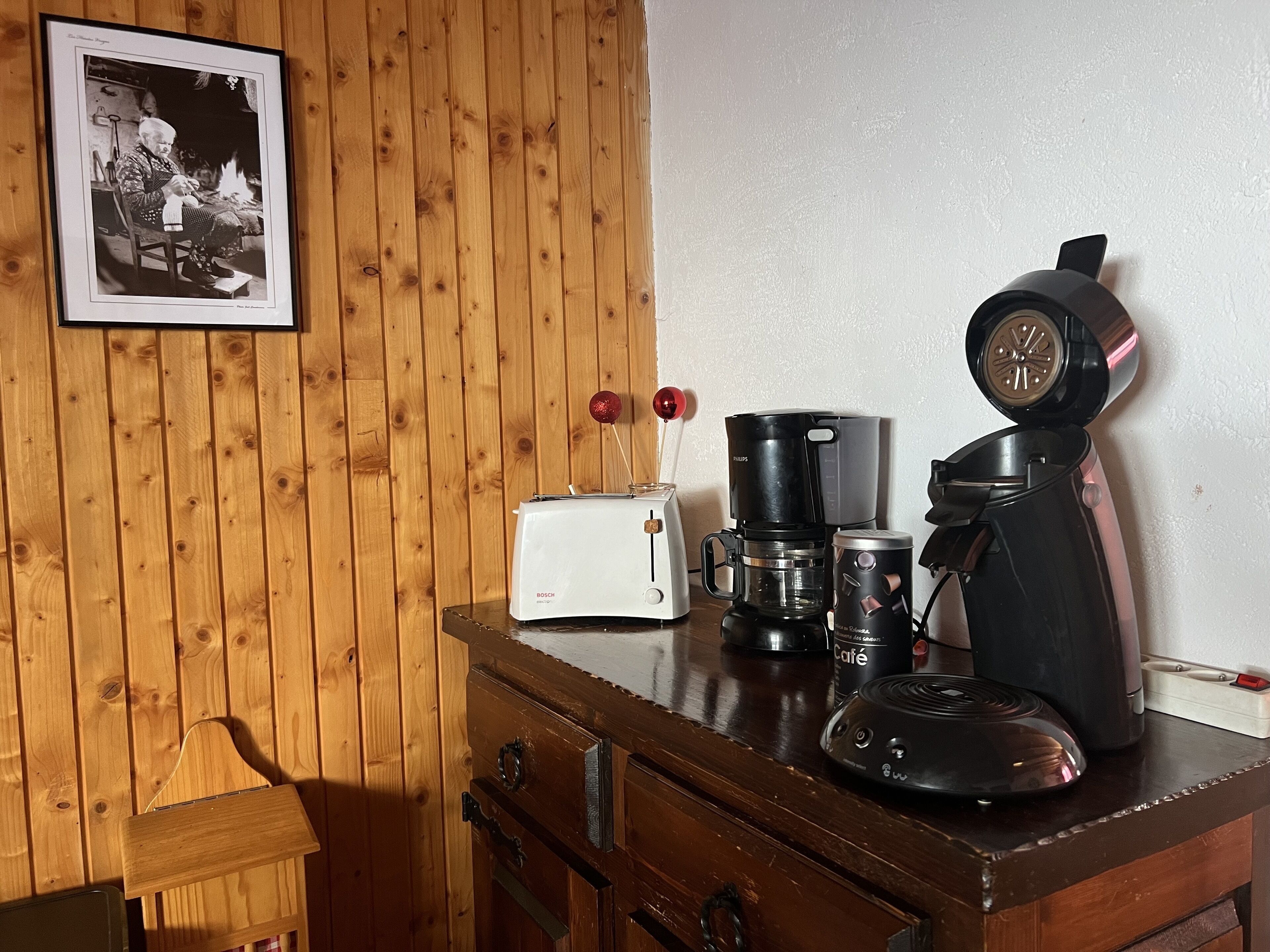 A wooden cabinet with a toaster, a coffee maker, and a mug on top.