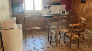A kitchen with wooden cabinets, a dining table with chairs, a microwave, a stove, and a window with natural light.
