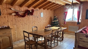 A cozy wooden dining room with a large table and chairs, a Christmas tree, and a wooden cabinet.