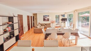 Een moderne woonkamer met een eethoek, houten vloeren en grote ramen.