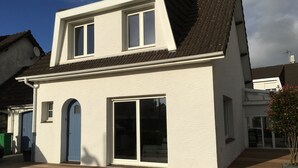 Ein zweistöckiges Haus mit weißer Fassade, einer blauen Tür und einem großen Schiebeglastür.
