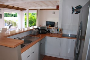 A modern kitchen with a wooden countertop, stainless steel appliances, and a view of greenery outside.