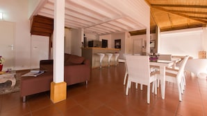 Amplia sala de estar con techo alto, una mesa de comedor con sillas, un sofá y una cocina al fondo.