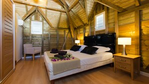 Un dormitorio con techo de madera, una cama con cabecera negra, una mesita de noche con una lámpara y una silla.