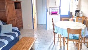 Een woonkamer met een bank, een houten tafel en een eethoek met stoelen en een tafelkleed.