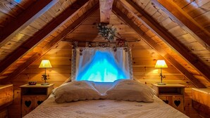 Een gezellig zolderkamer met een groot bed, twee bedlampen en uitzicht op een verlicht blauw raam.