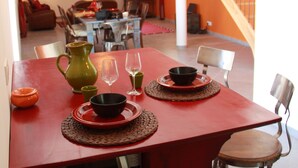 A dining area with a red table, chairs, and a pitcher. There is a staircase in the background.