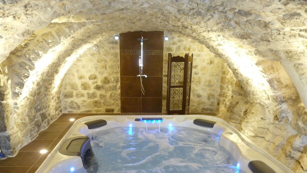 A hot tub in a stone-walled room with a wooden door and a small window.