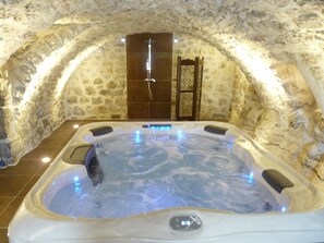 Ein Whirlpool in einem Raum mit Steinwänden, einer Holztür und einem kleinen Fenster.