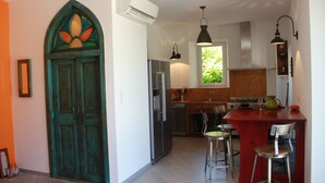 A kitchen with a central island, bar stools, a refrigerator, and a window with a view of greenery.