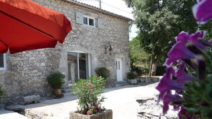 A stone building with a window, a door, and a small garden with plants and flowers.