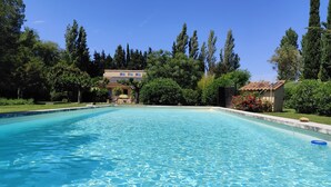 Une piscine aux eaux cristallines, entourée de verdure, avec un bâtiment visible au loin.