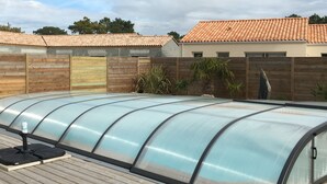 Une serre dotée d’une structure et d’un toit en verre incurvé, construite sur une terrasse en bois.