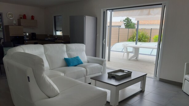 Un salon moderne avec un canapé blanc, une table basse et une porte-fenêtre coulissante donnant sur une terrasse extérieure.