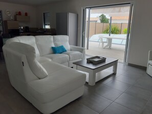 A modern living room with a white sofa, a coffee table, and a sliding glass door leading to an outdoor patio. - Turquoise villa - private pool, wooden terrace (ST JEAN DE MONTS)